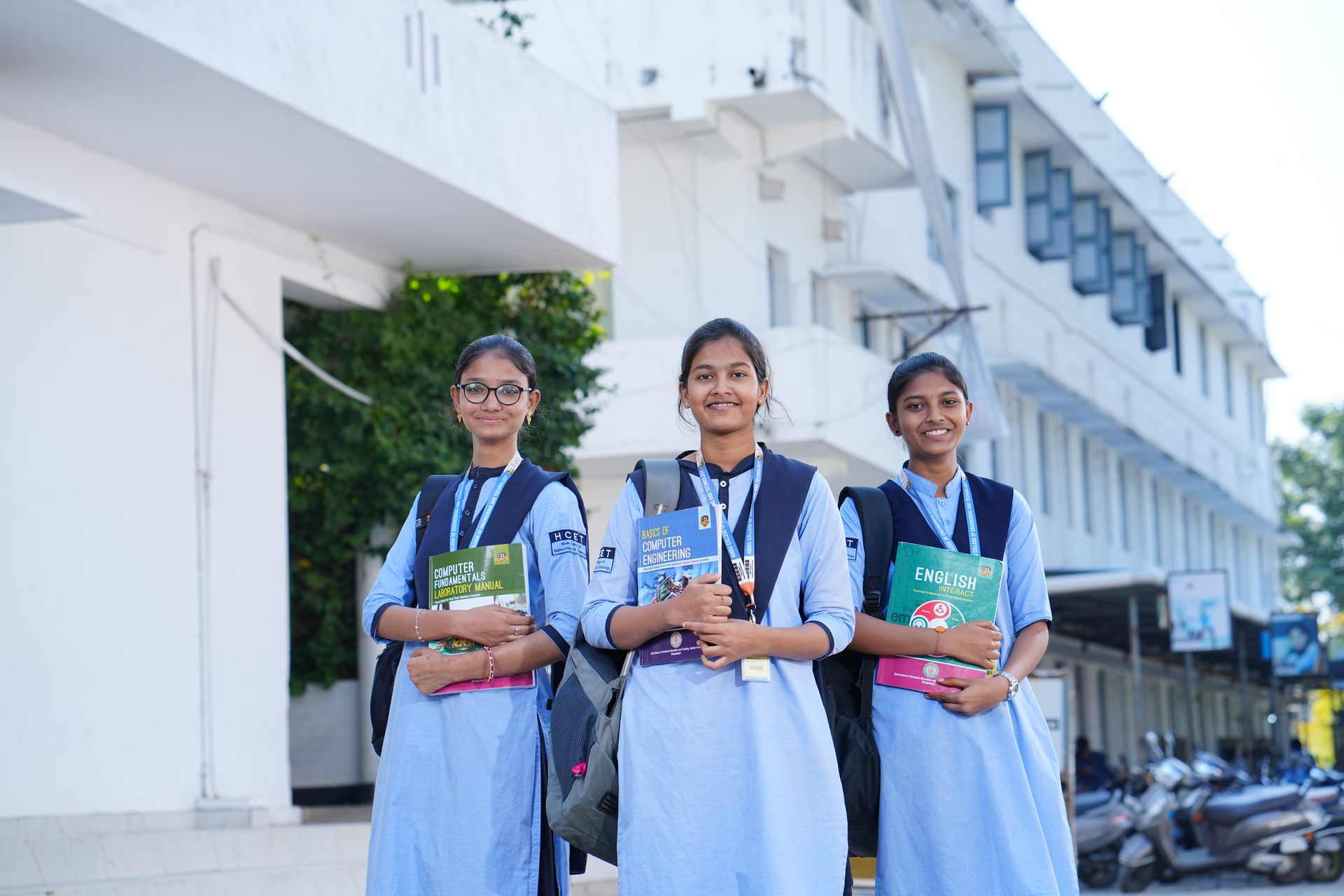 Three students holding their books outside the college building